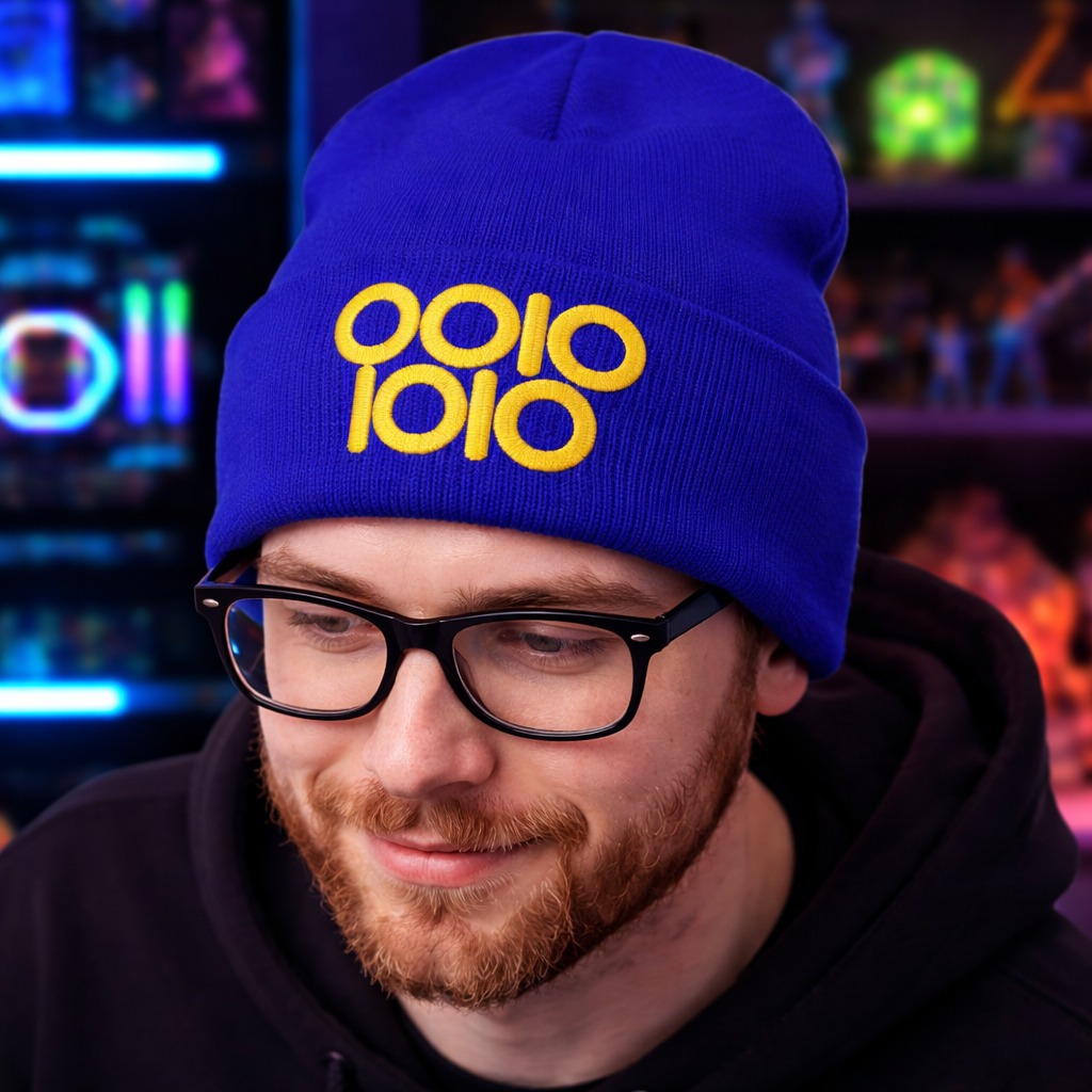 A royal blue beanie embroidered with “0010 1010” in gold thread, styled in a neon-lit gaming setup with shelves of collectibles and soft RGB lighting in the background.