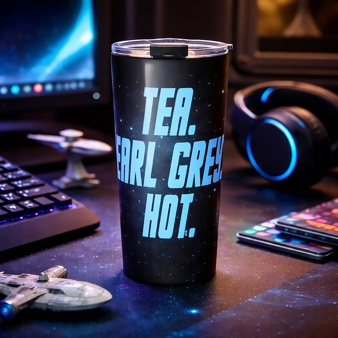 A stainless steel 20 oz tumbler featuring the phrase “Tea. Earl Grey. Hot.” in bold blue lettering sits on a sci-fi-inspired desk setup with a keyboard, glowing headphones, and space-themed collectibles, giving the scene a starship-ready geek aesthetic.