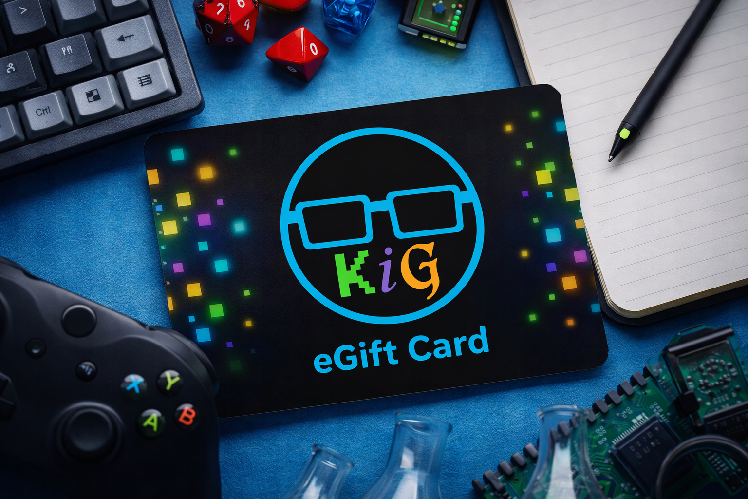 A Keep It Geek eGift Card featuring the KiG glasses logo, styled on a geek desk with a mechanical keyboard, gaming controller, dice, and tech accessories — the perfect gift for every fandom.