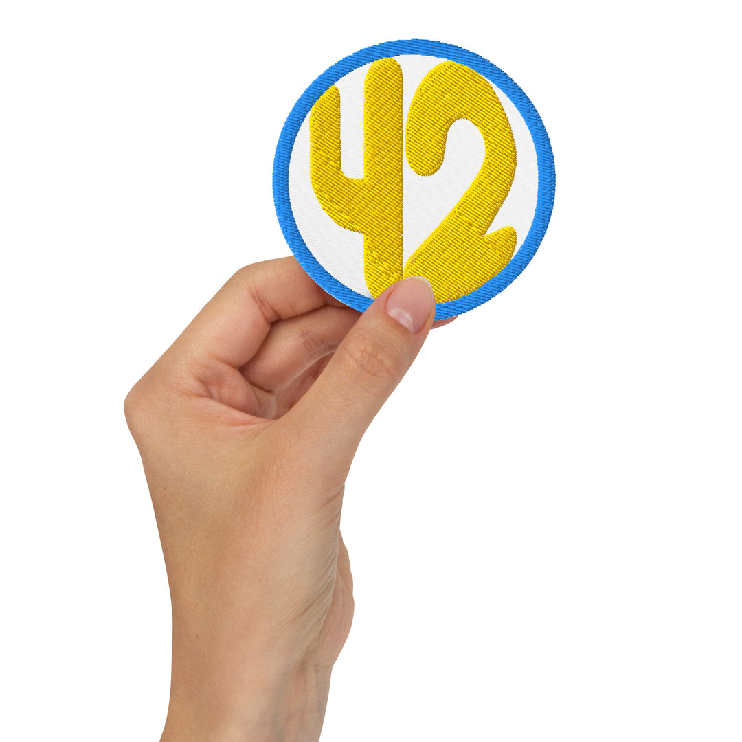 Hand holding a 3-inch embroidered 42 circle patch with gold numbers on a white background and blue border.