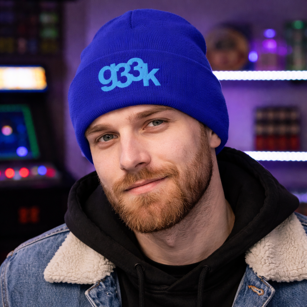 Model wearing a royal blue g33k leetspeak embroidered cuffed beanie in a geek-themed room with arcade lighting