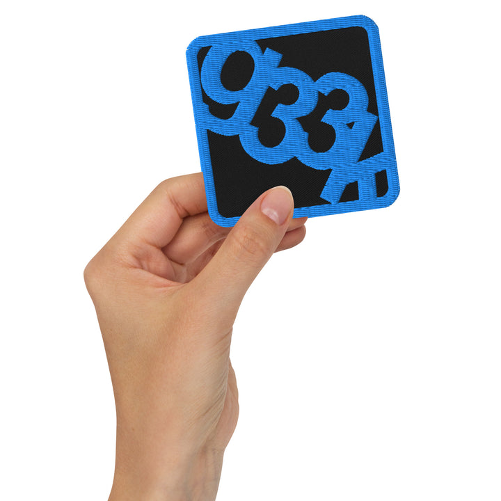 Black square embroidered g33k leetspeak patch held in hand