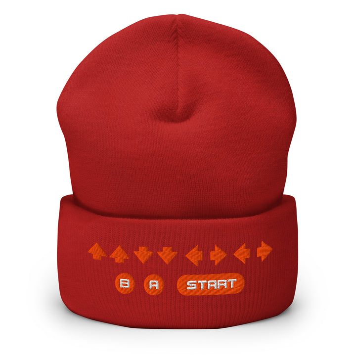 Front view of a red cuffed beanie displaying embroidered retro cheat code arrows with B, A, and START symbols on the cuff.