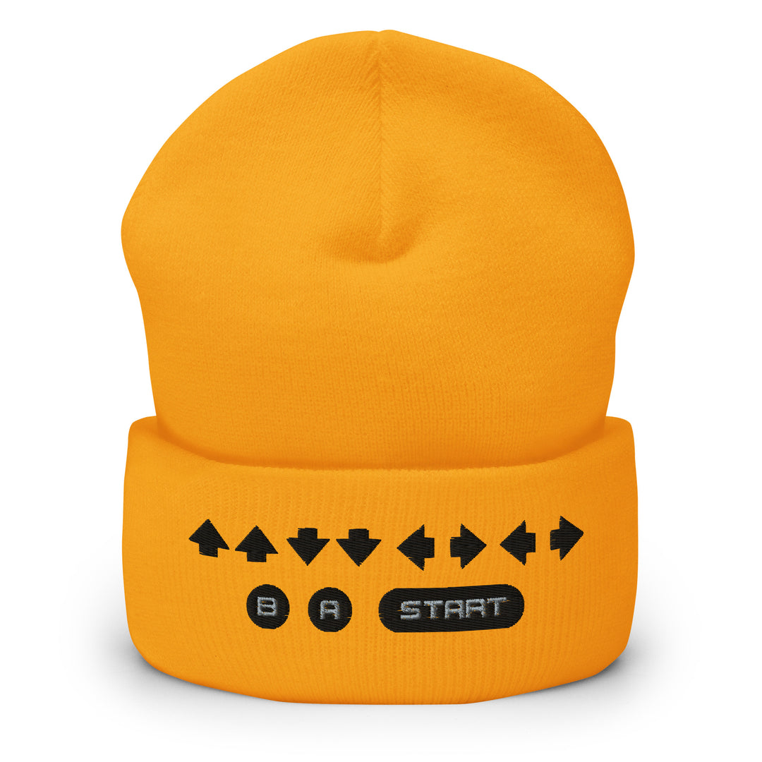 Front view of a yellow cuffed beanie displaying embroidered retro cheat code arrows and classic B, A, START icons on the cuff.