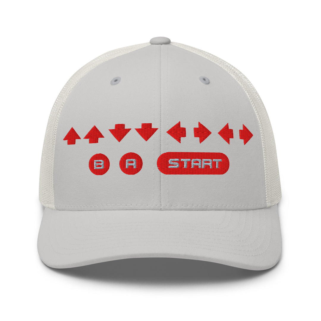 Front view of a silver snapback trucker cap with red embroidered retro cheat code arrows and B A START buttons on the front panel