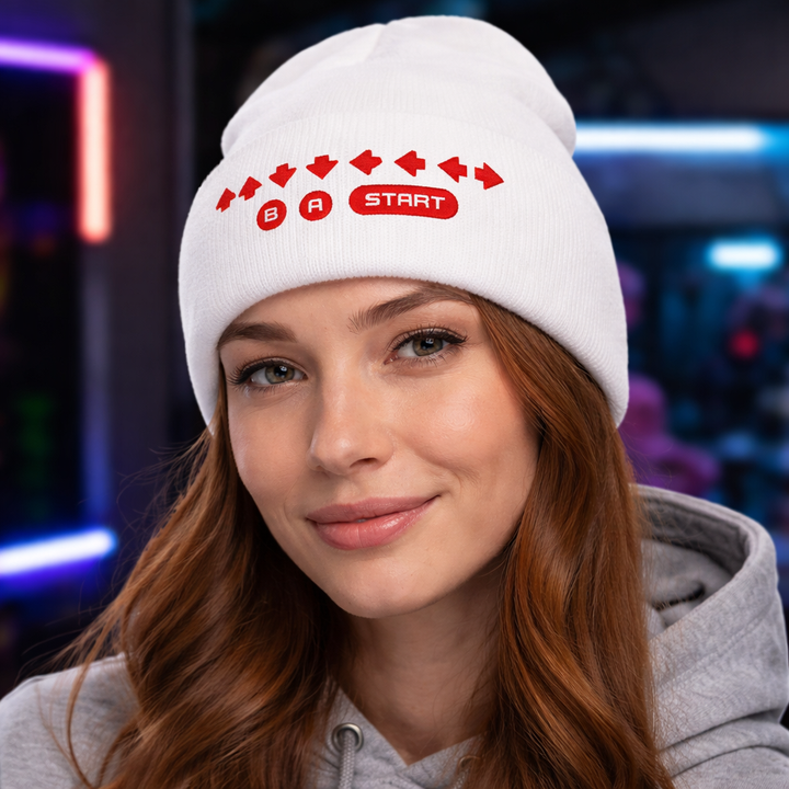 Lifestyle model image showing a person wearing the white Retro Cheat Code Embroidered Cuffed Beanie, featuring crisp red embroidered arrow symbols with B, A, and START icons on the folded cuff.