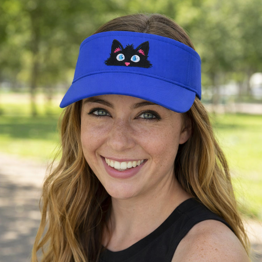 Woman wearing a blue embroidered visor featuring the Frazzled peeking black cat personality, shown in an outdoor lifestyle setting.