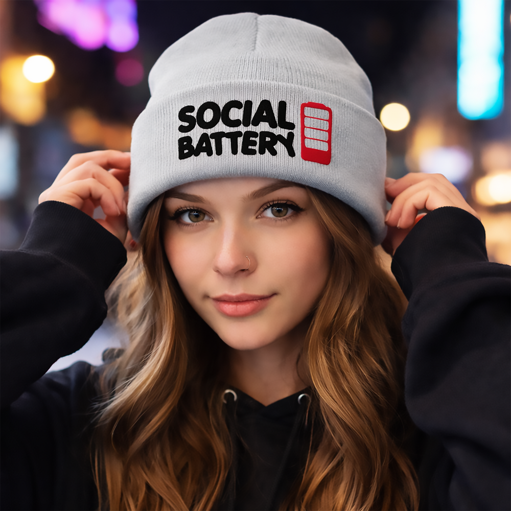 Model wearing a heather gray cuffed beanie embroidered with “Social Battery” and a red low-battery icon—because small talk has a limited runtime.